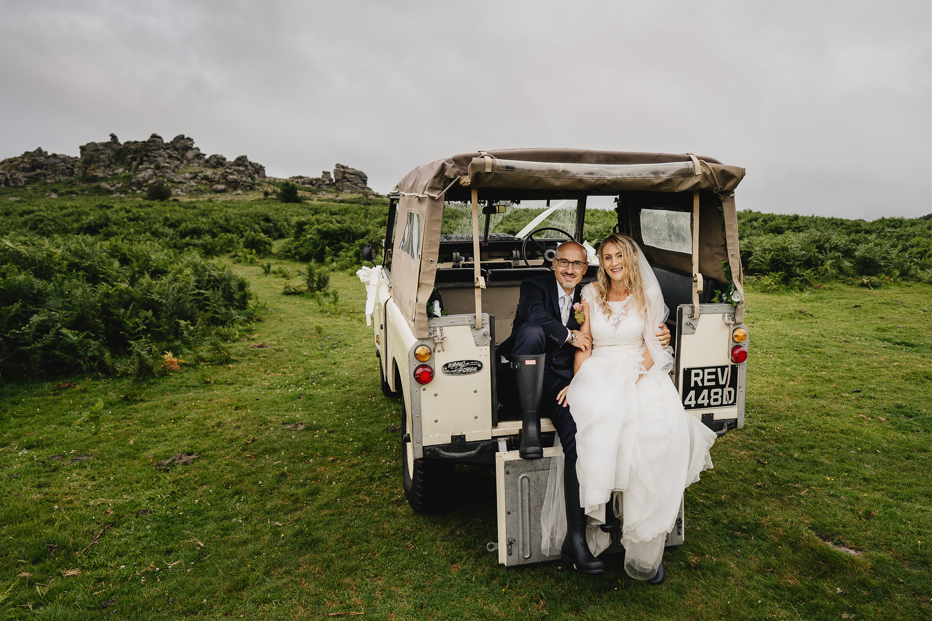 A bride and groom sitting in the back of a landrover on Dartmoor