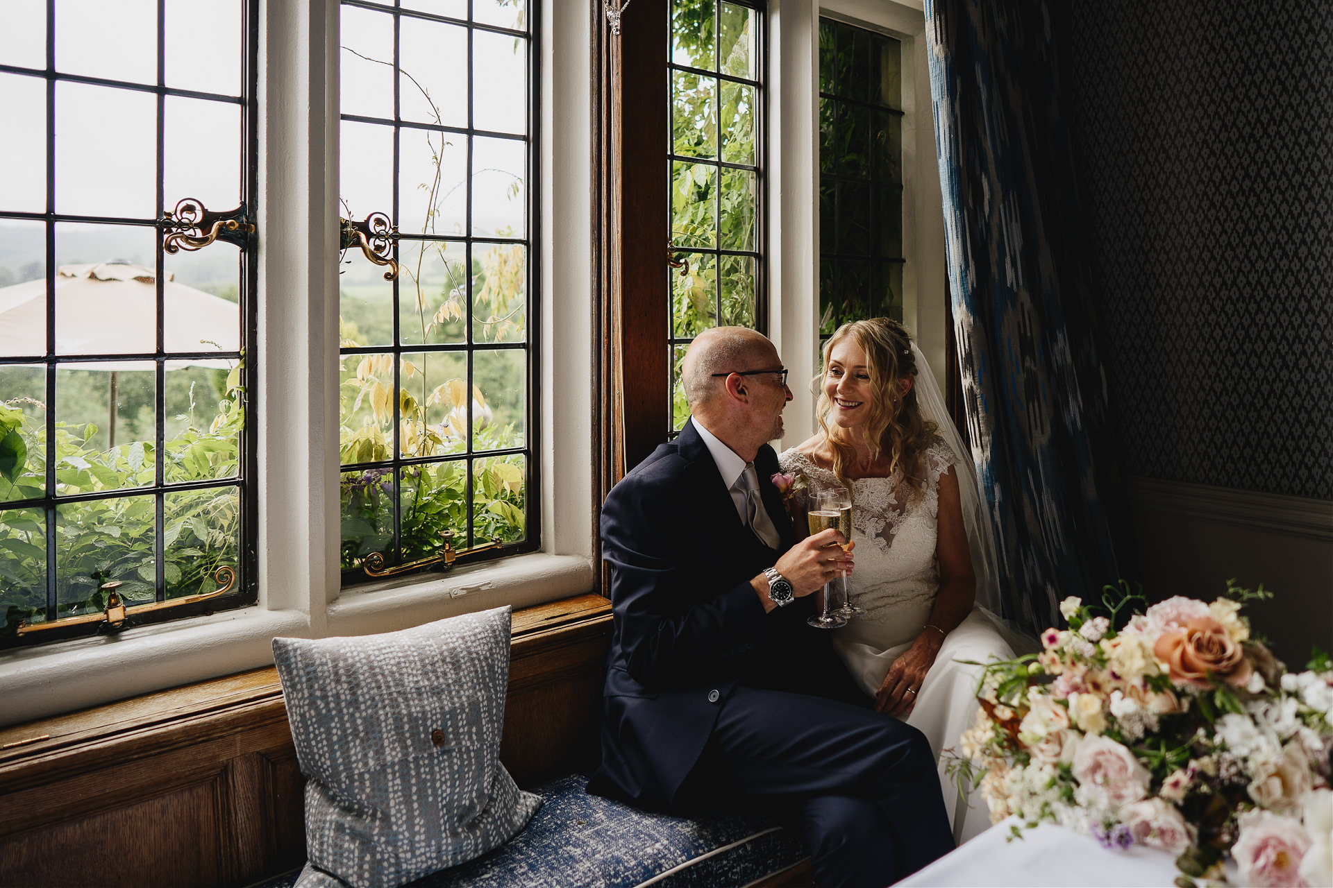 Bride and groom just married, sitting on a window seat together smiling at Bovey Castle