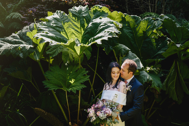 Tiny Cornwall wedding with bride and groom posing by huge leaves
