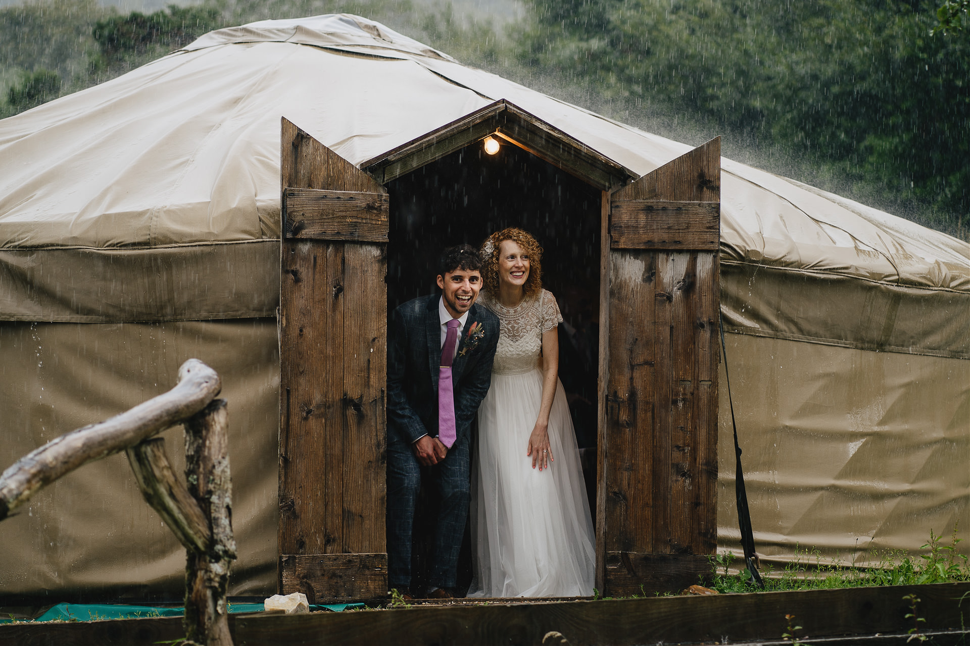 A bride and groom peeking out from a yurt with rain hammering down all around them on a really wet and rainy wedding day at River Cottage