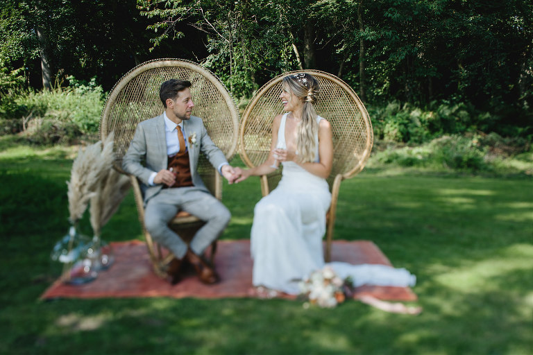 Bride and groom at a relaxed boho wedding sitting outdoors in peacock chairs