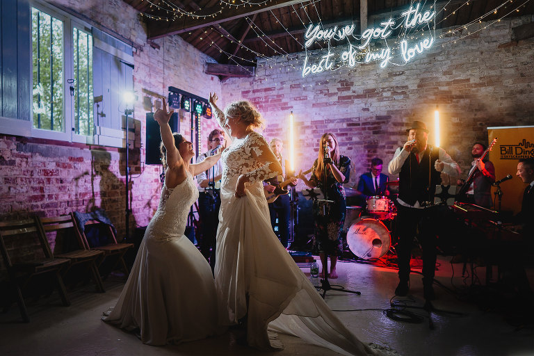 Wedding photo of two brides dancing together with a band playing behind them