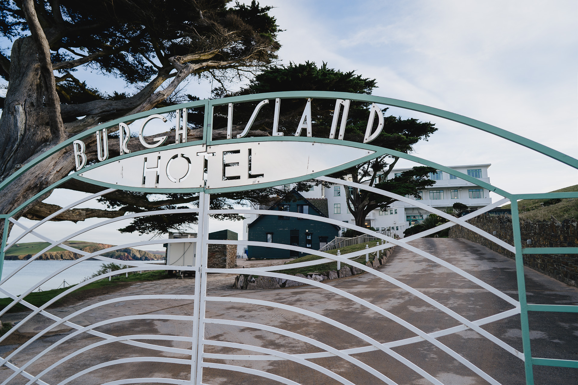 The front gates to Burgh Island Hotel with art deco lettering and the hotel driveway behind