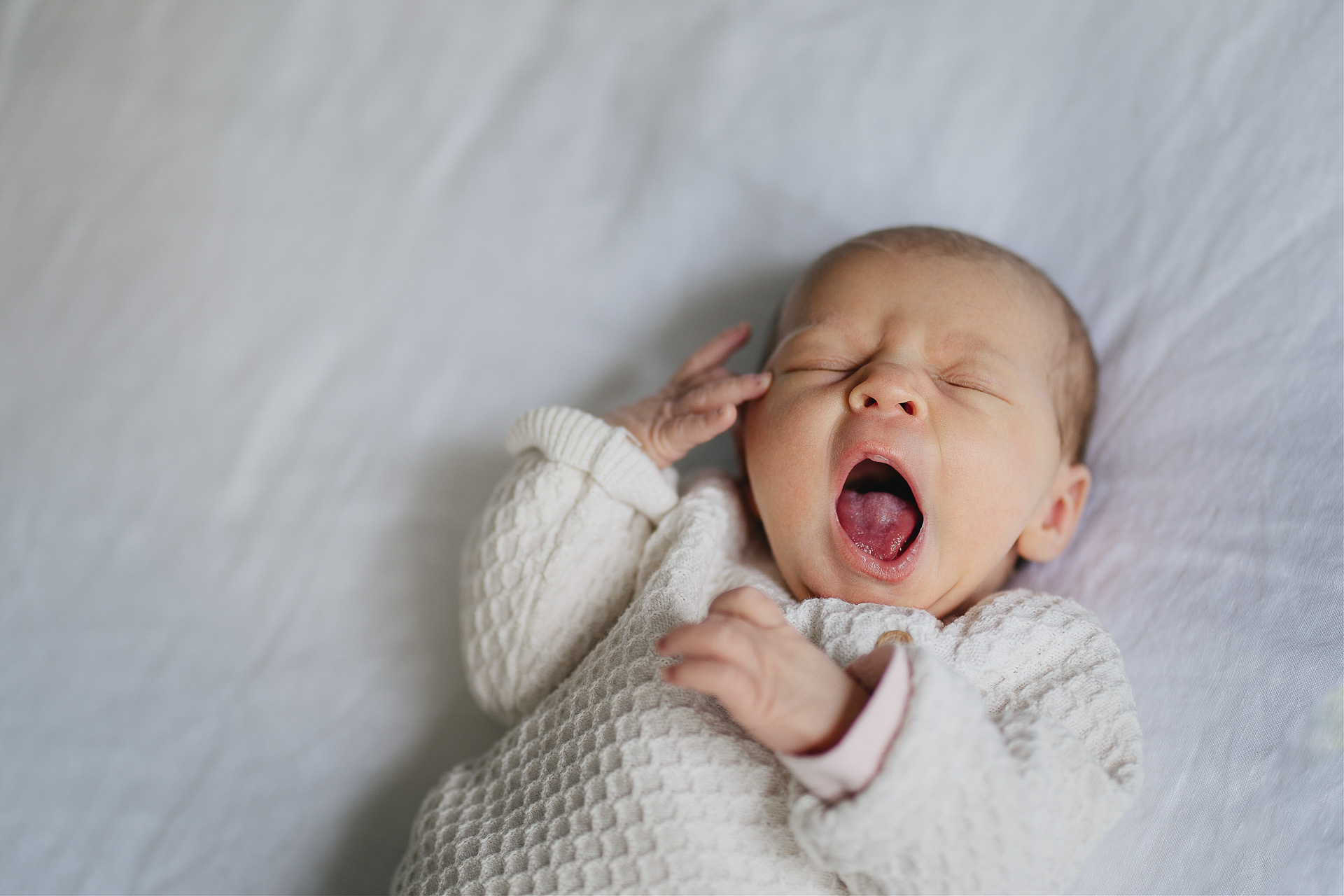 A yawning newborn baby lying on a bed at home