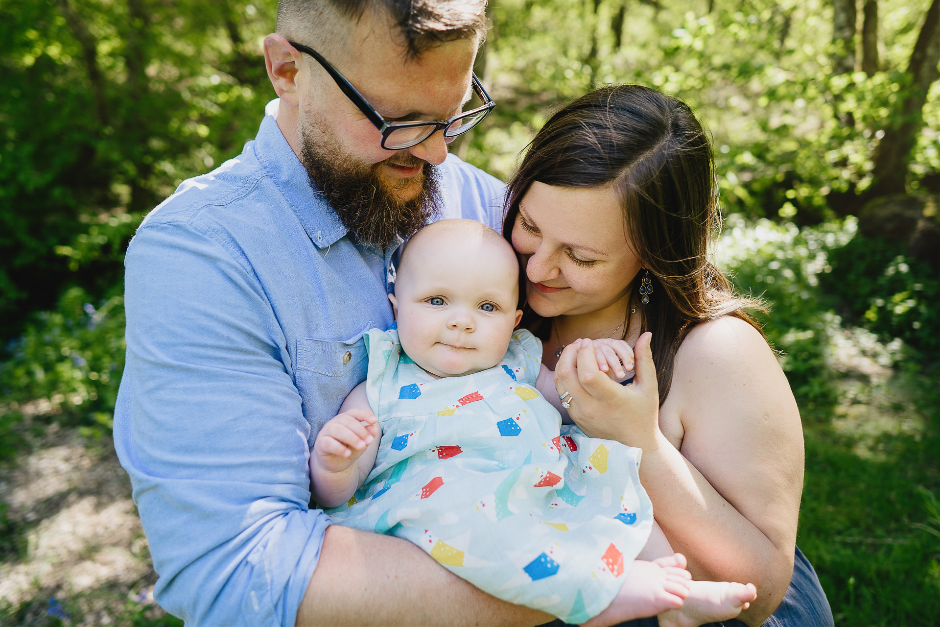Family photograph of parents cuddling a baby in woodland