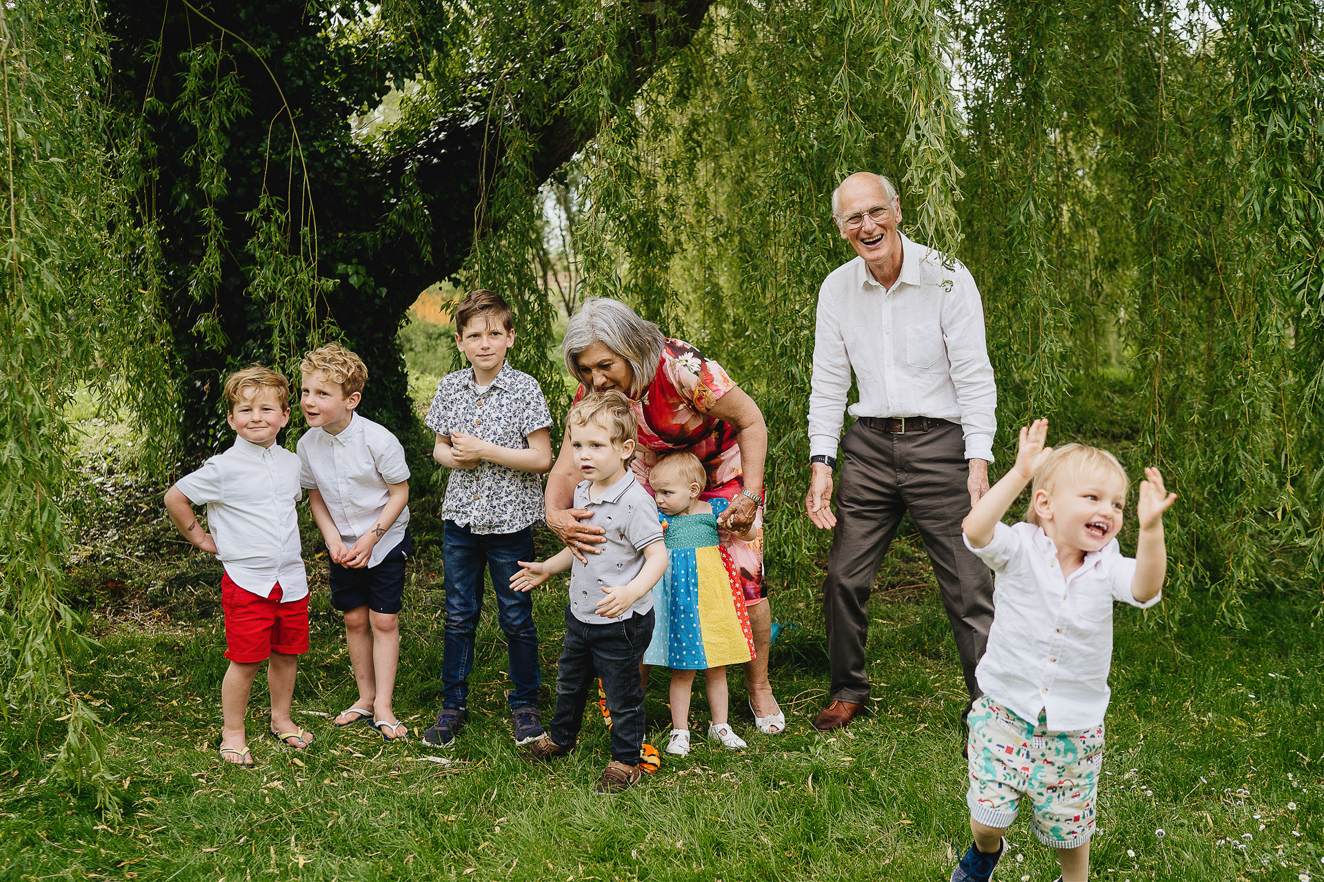 grandparents laughing at a chaotic situation with young grandchildren trying to pose for a photograph