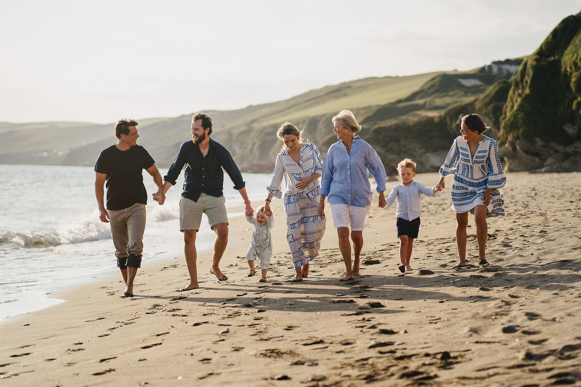 an extended family walking hand in hand along a beach and laughing
