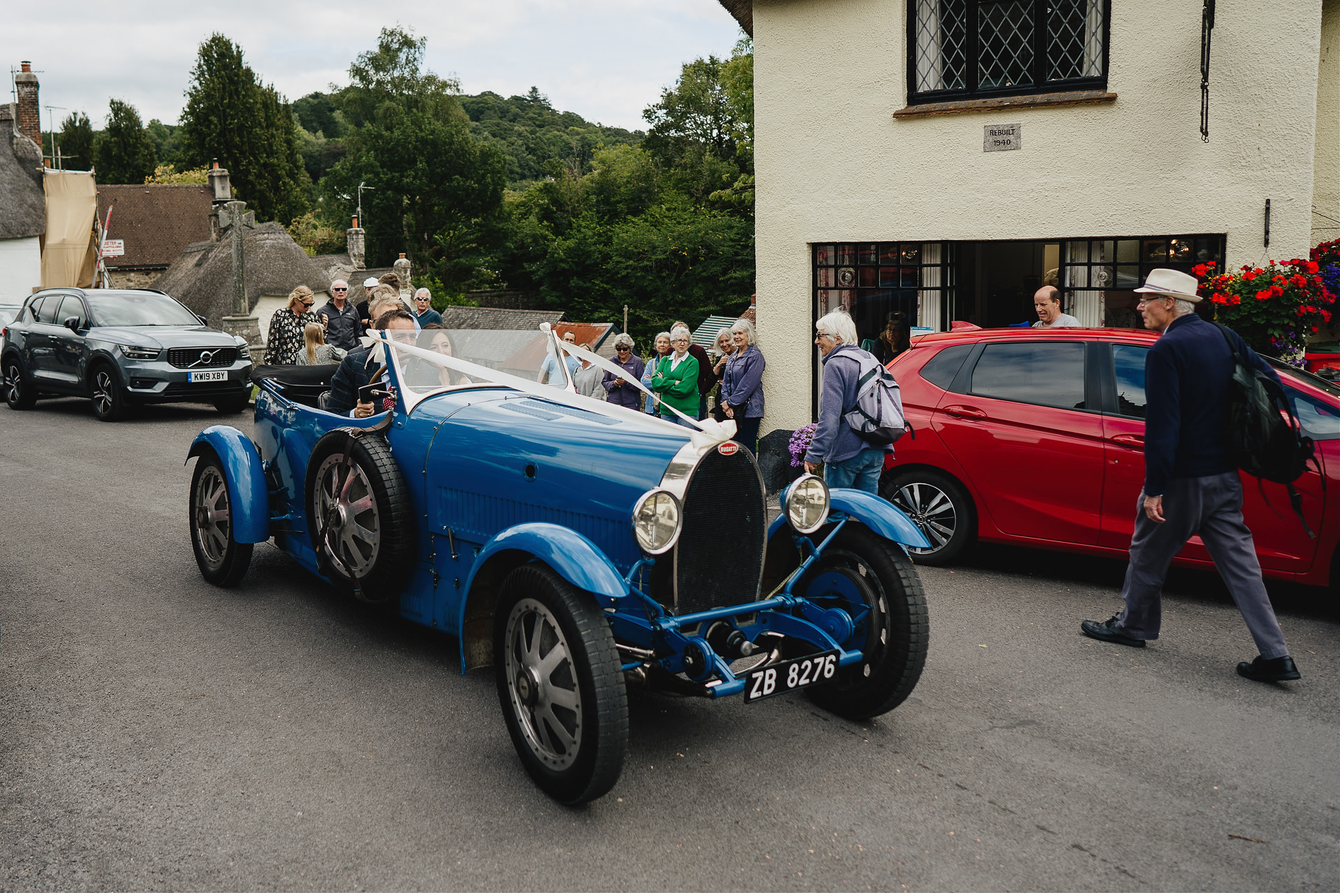 Bride arriving along a village street in an incredible vintage blue car