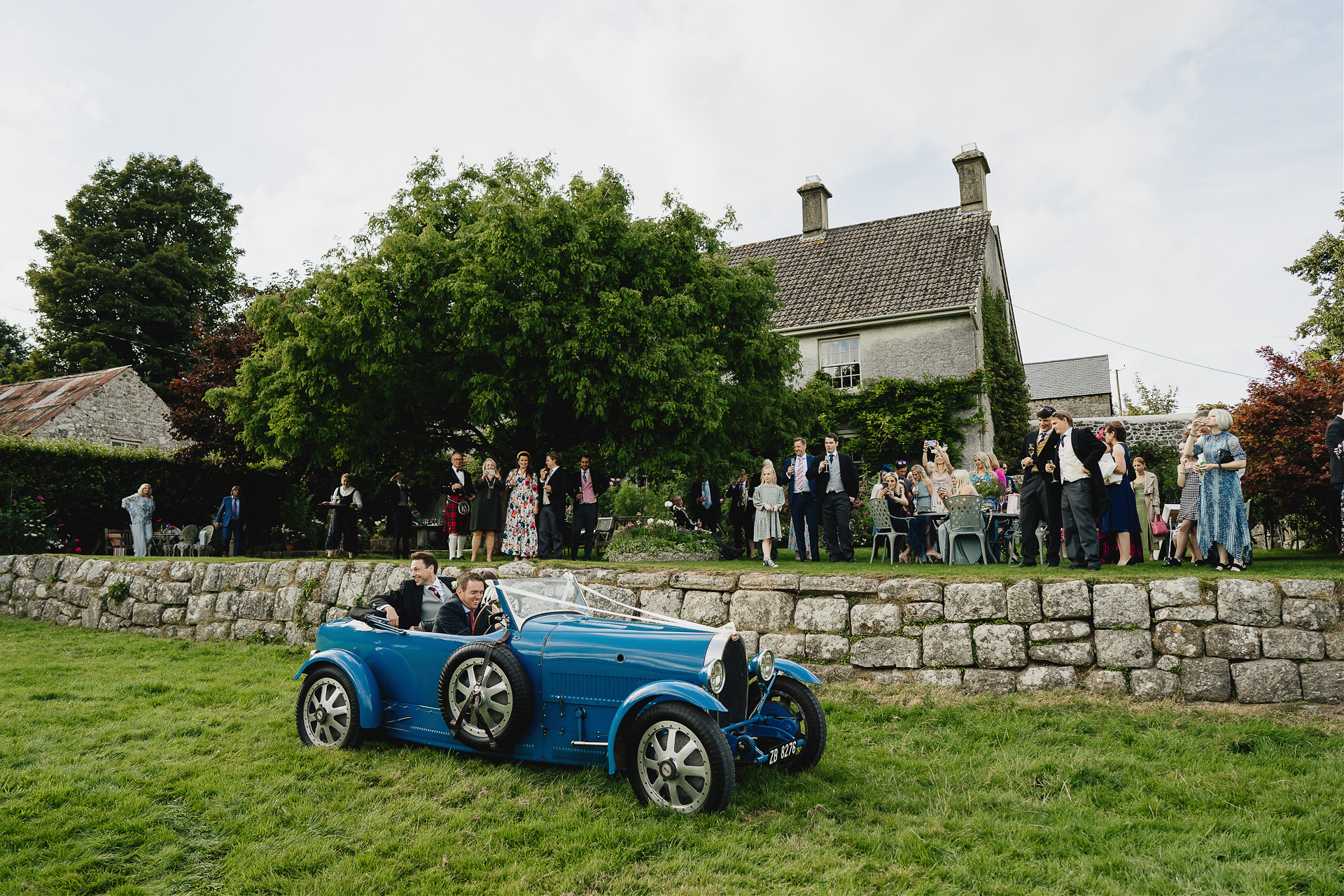 Bride and groom arriving at a beautiful barn venue on Dartmoor with guests watching from the lawn 