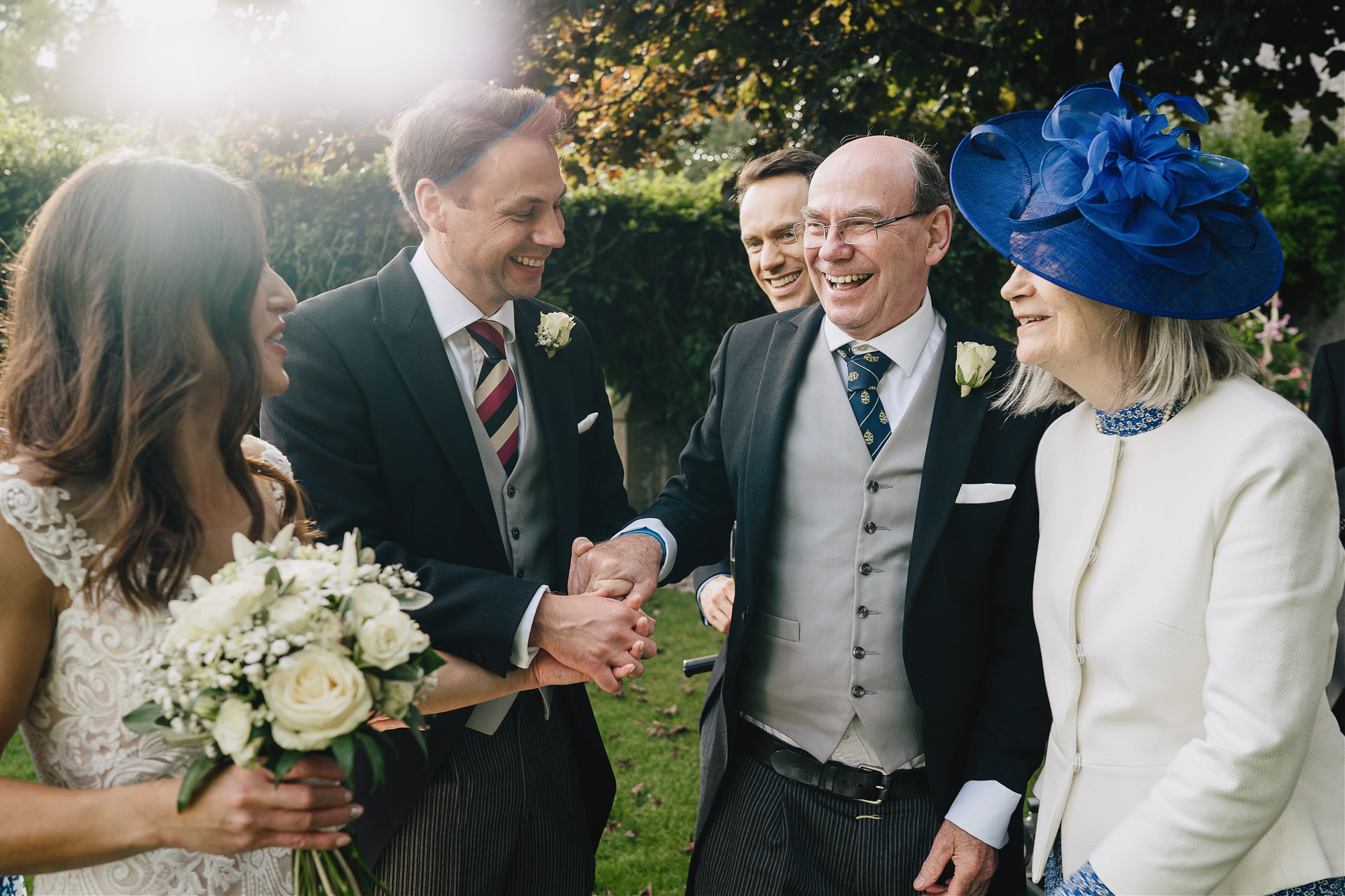 Wedding guests laughing together in a beautiful garden with sunlight behind