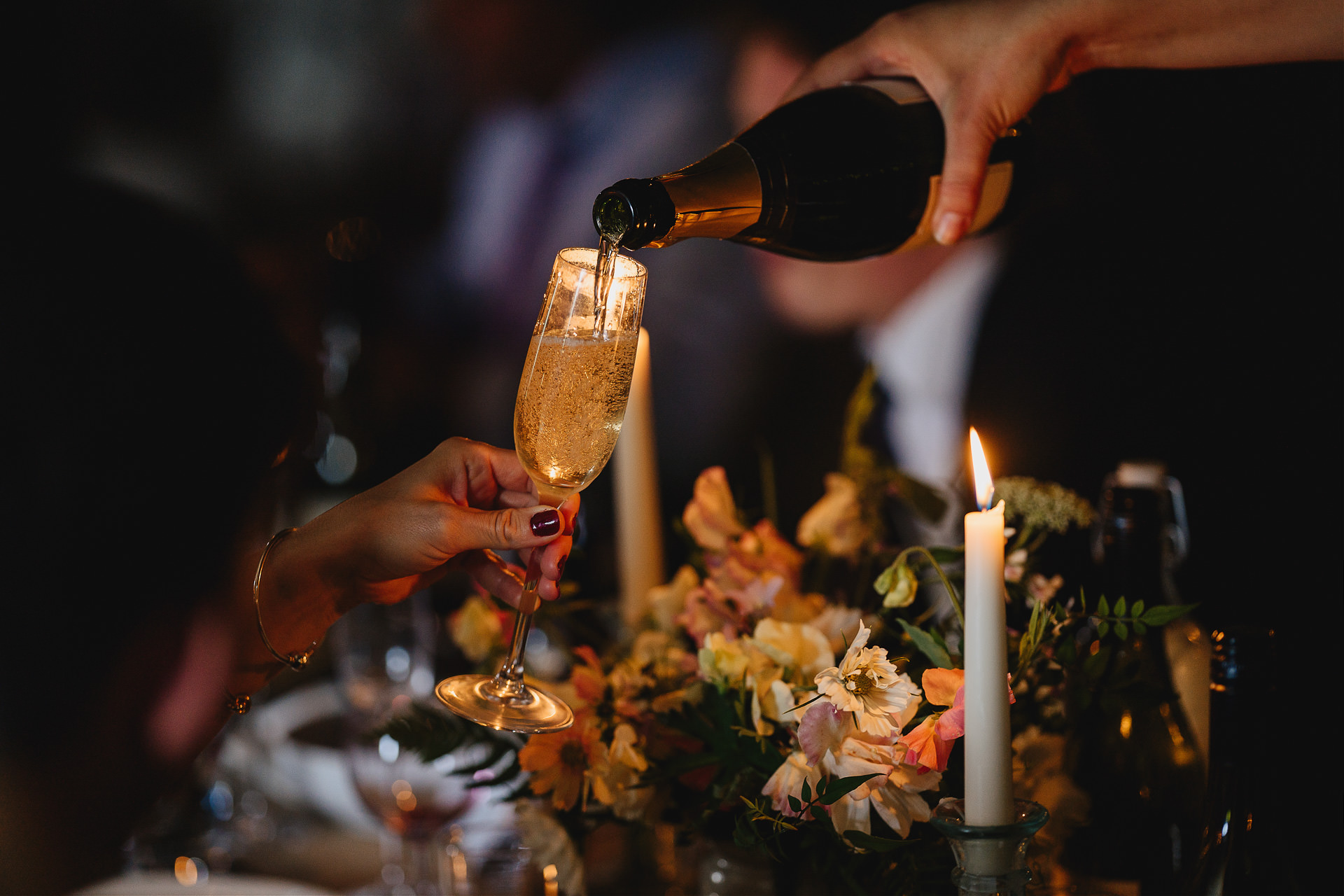 Champagne being poured into a glass in a dark barn with candles lit