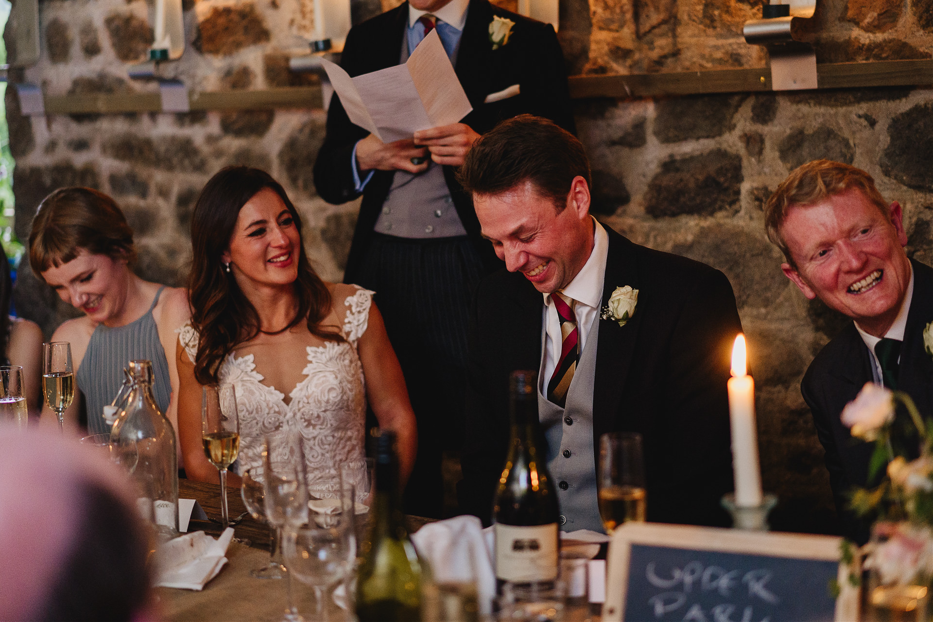 Bride and groom laughing at wedding speeches in a barn