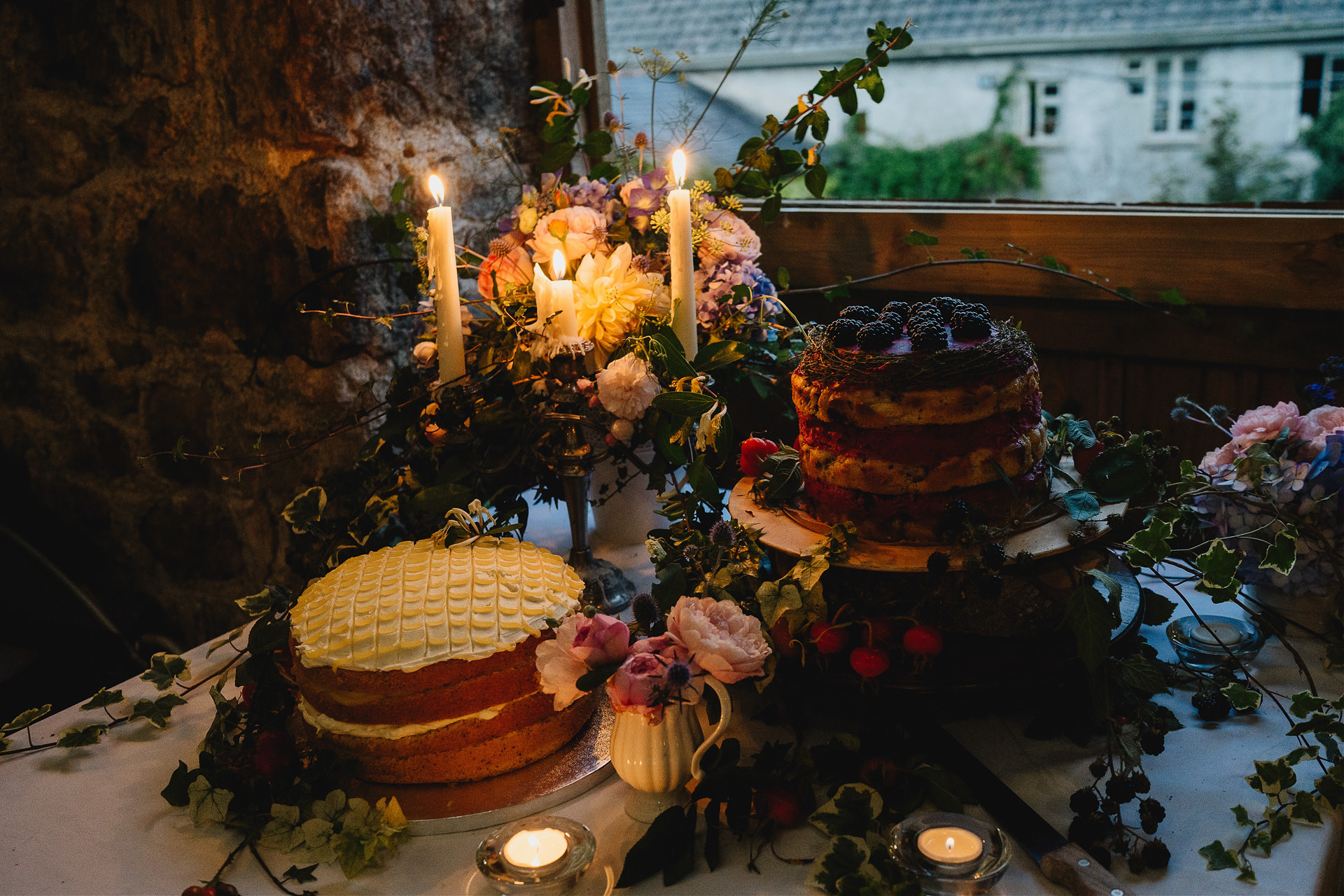 Cakes with candles lit and beautiful foliage decorations in a wedding barn