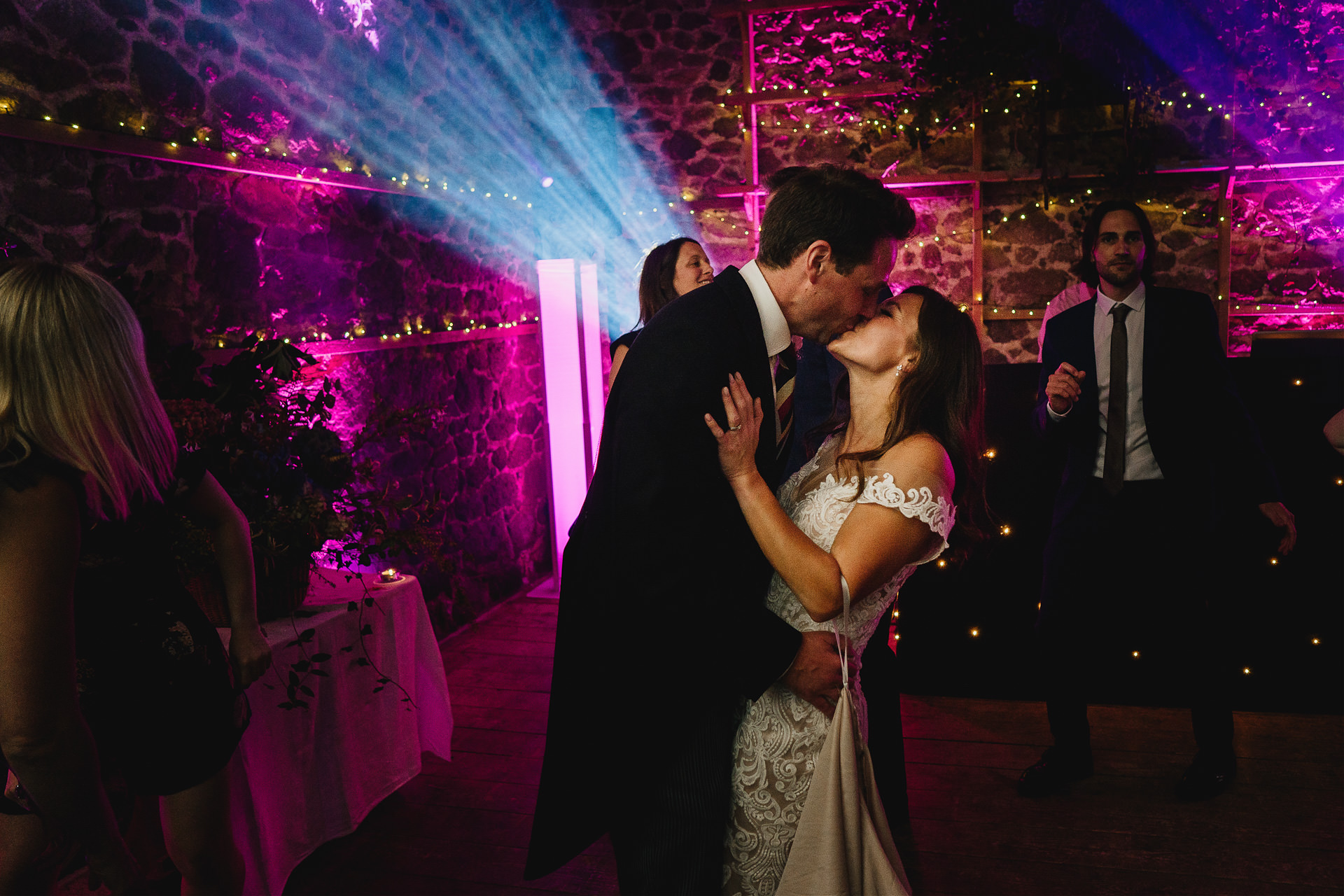 Bride and groom kissing on a dance floor with real wow factor lighting around them in a wedding barn venue