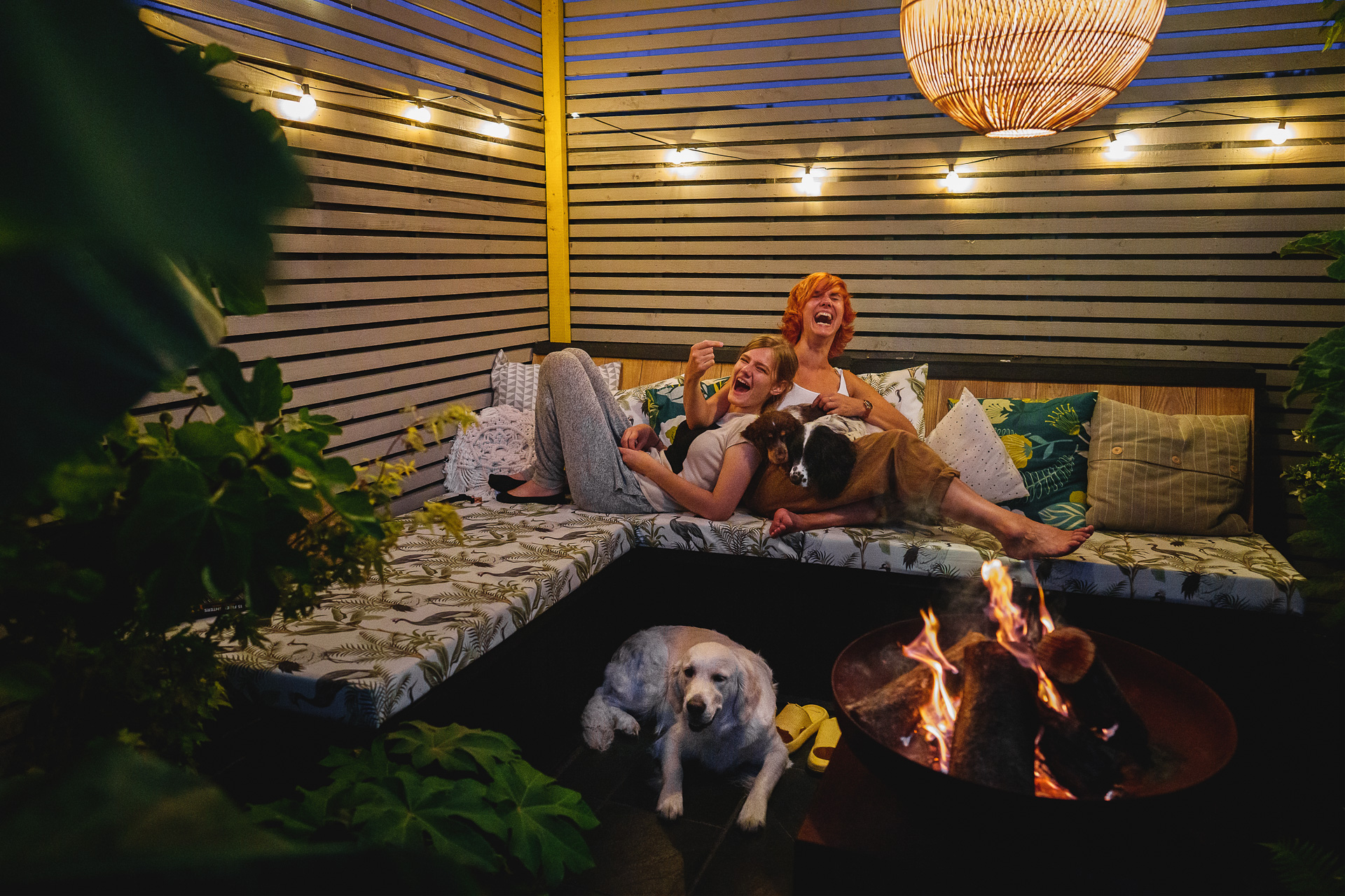 A mother and teenage daughter sitting by a fire pit and laughing together with dogs. 