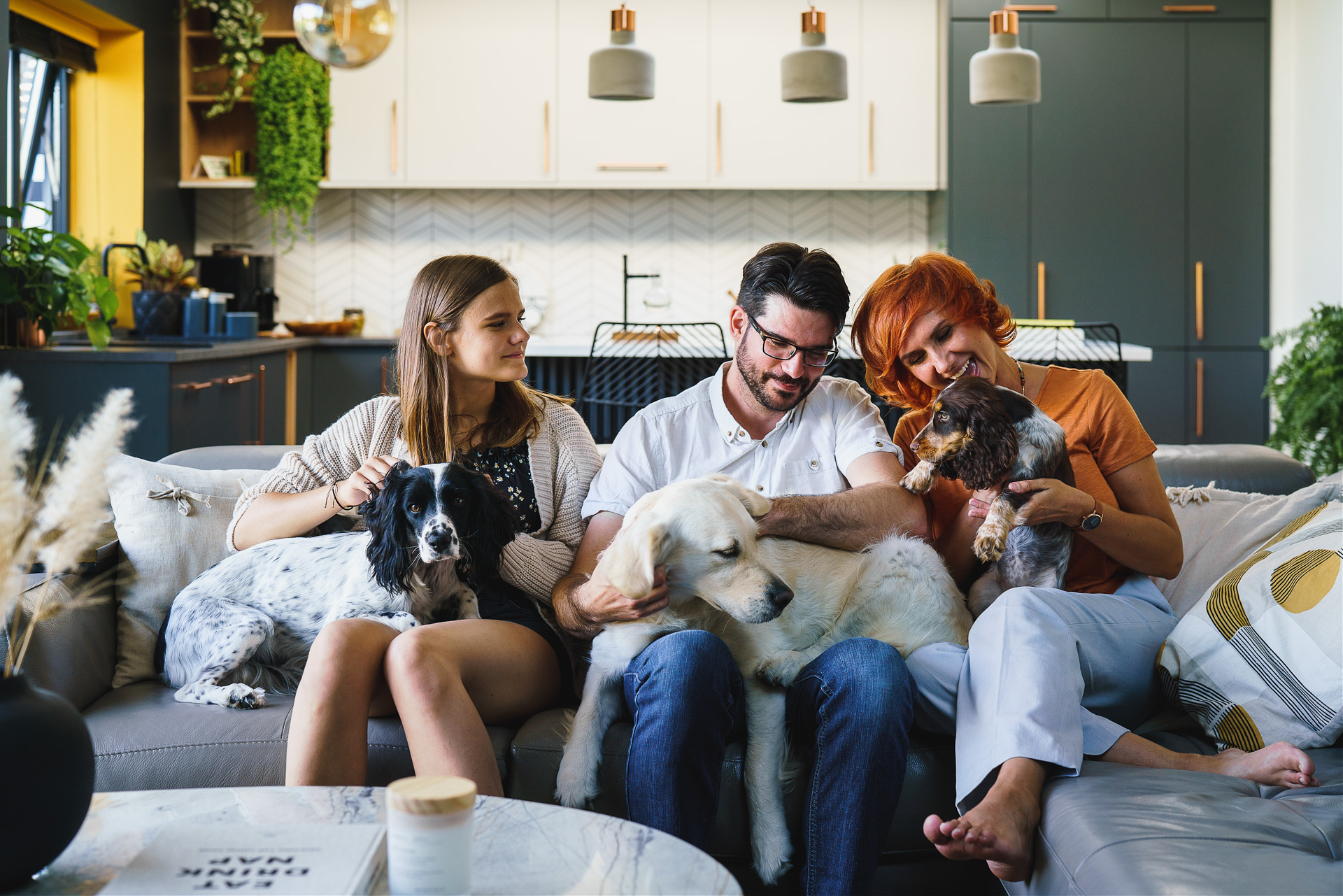 A family sitting with their dogs on a grey sofa inside a beautiful house