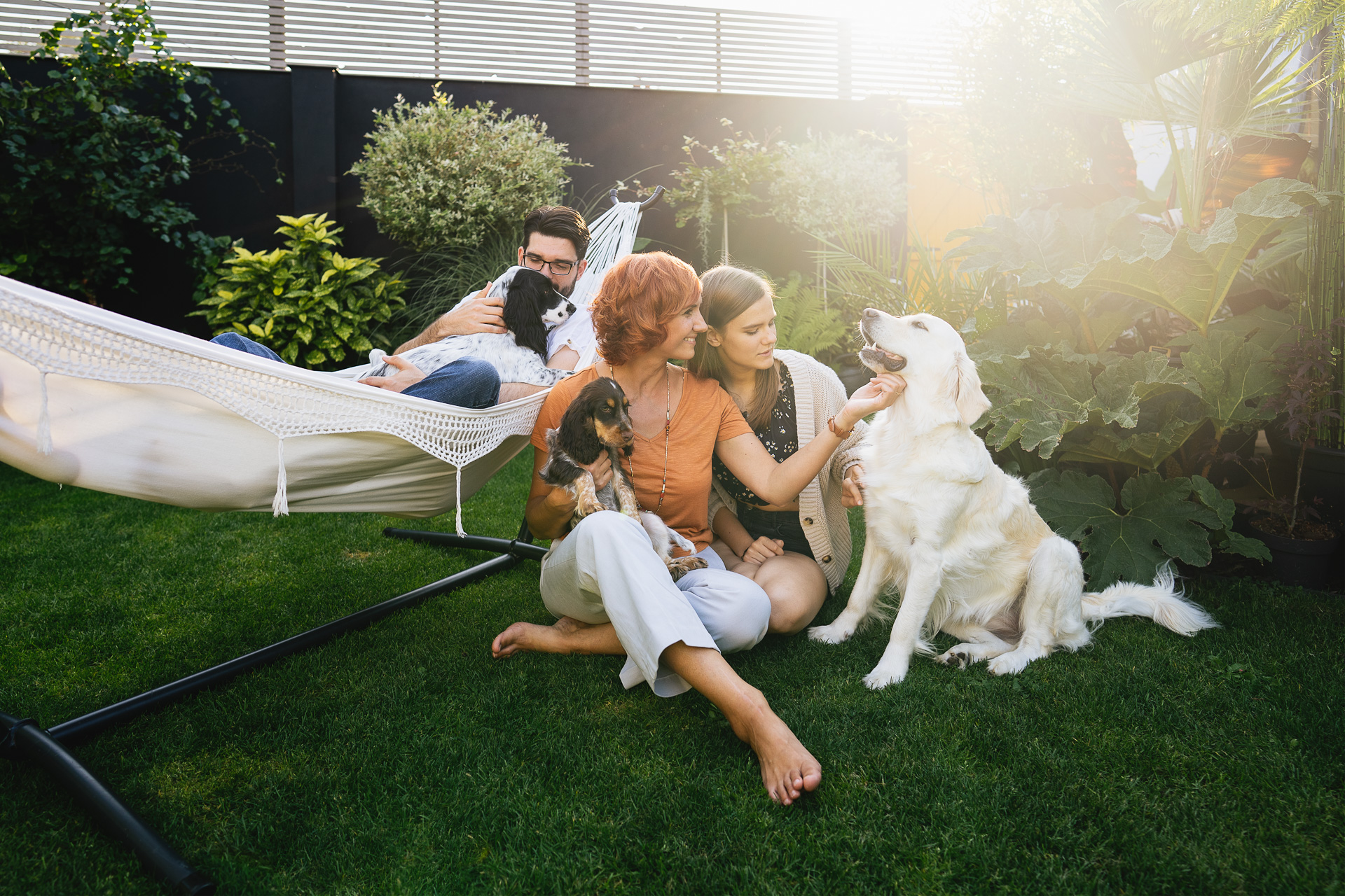 A family relaxing with their dogs, sitting on grass and a hammock in a beautiful garden