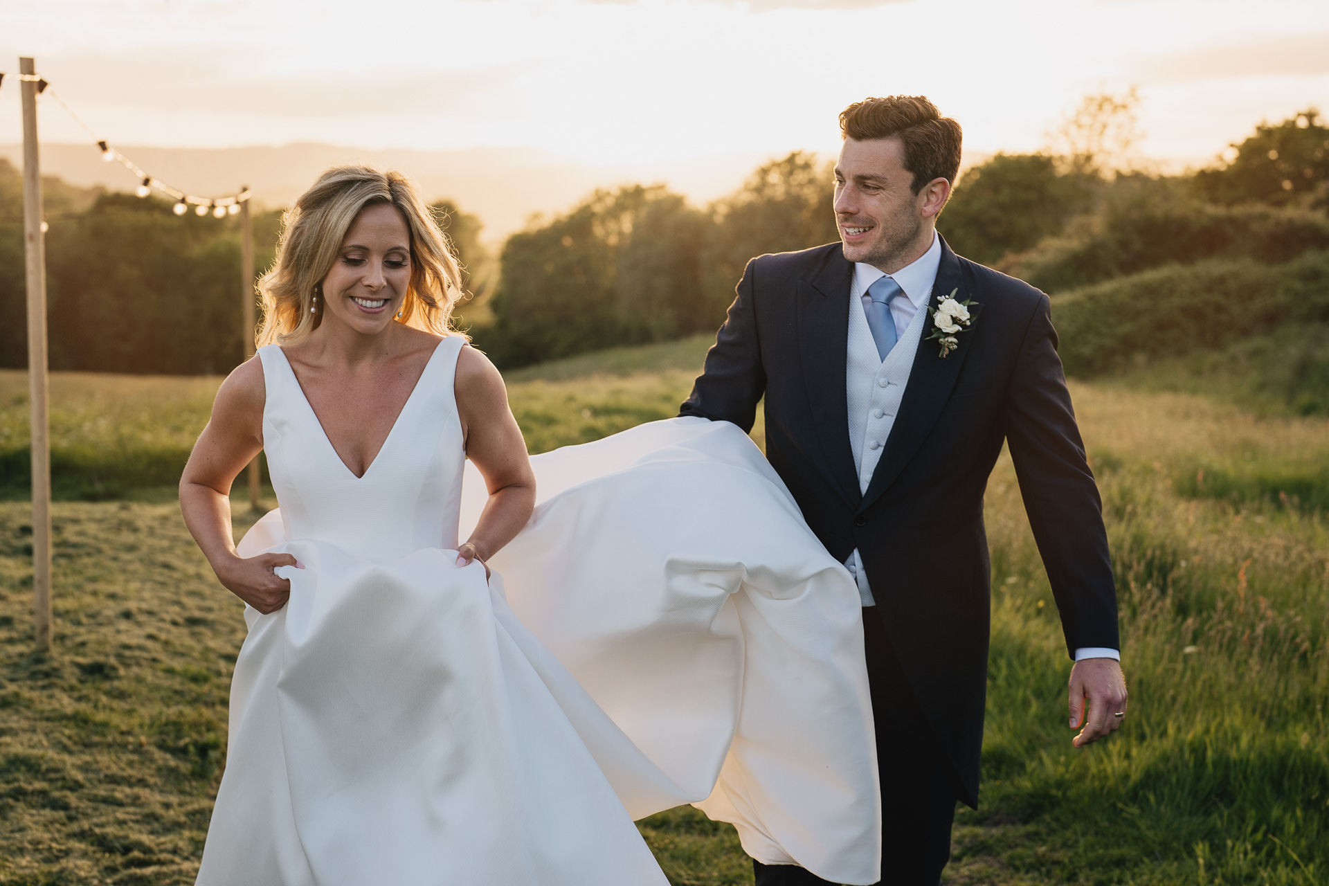 Bride and groom walking across the fields at River Cottage in the sunset
