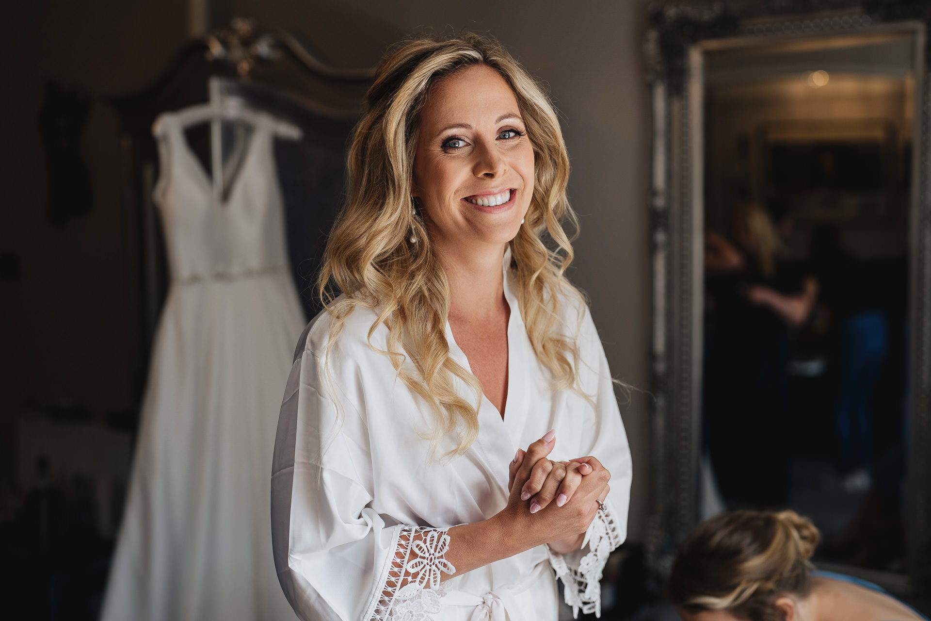 A smiling bride to be, with a wedding dress hanging behind her