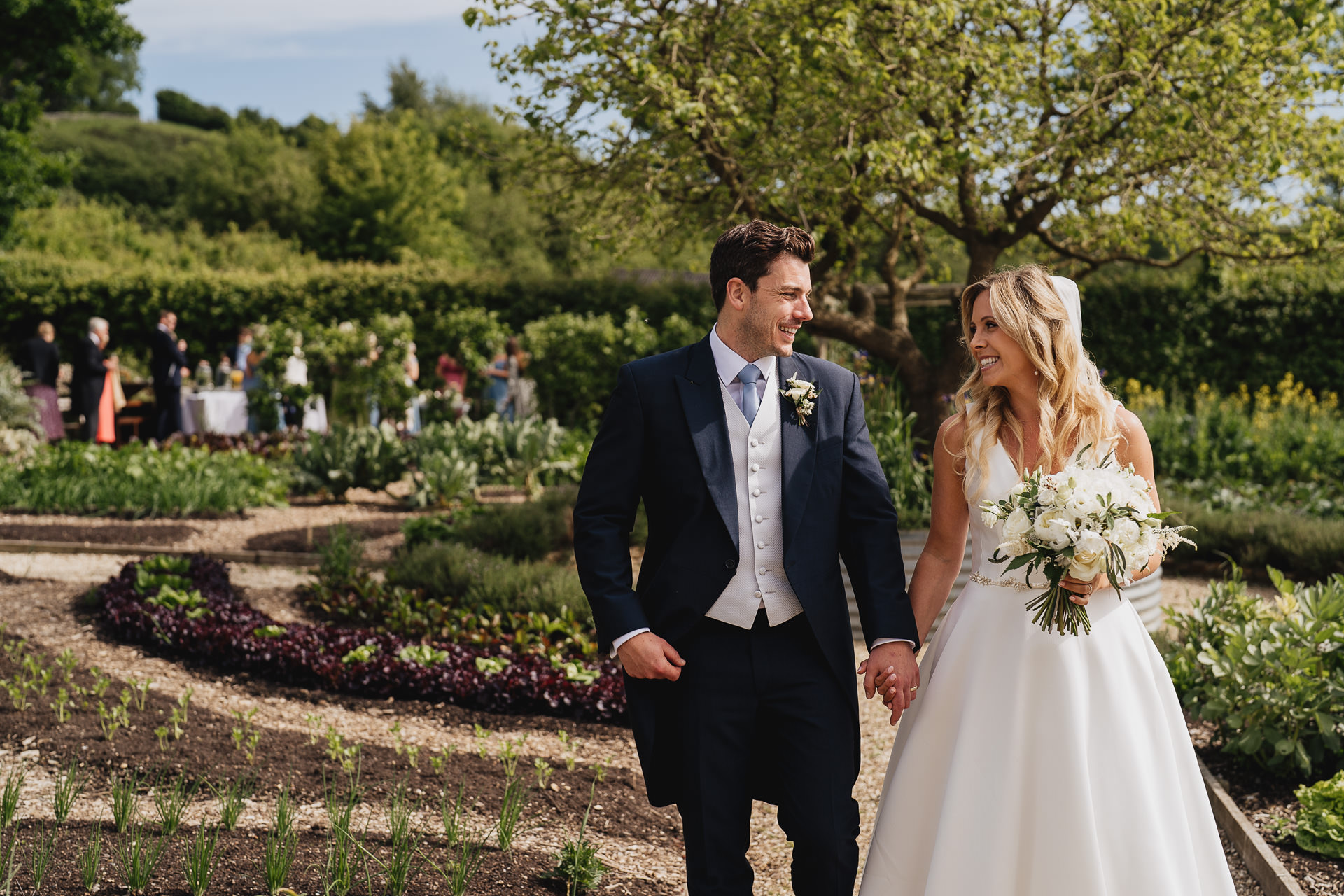 Bride and groom walking through the kitchen garden smiling at each other  during their wedding at River Cottage