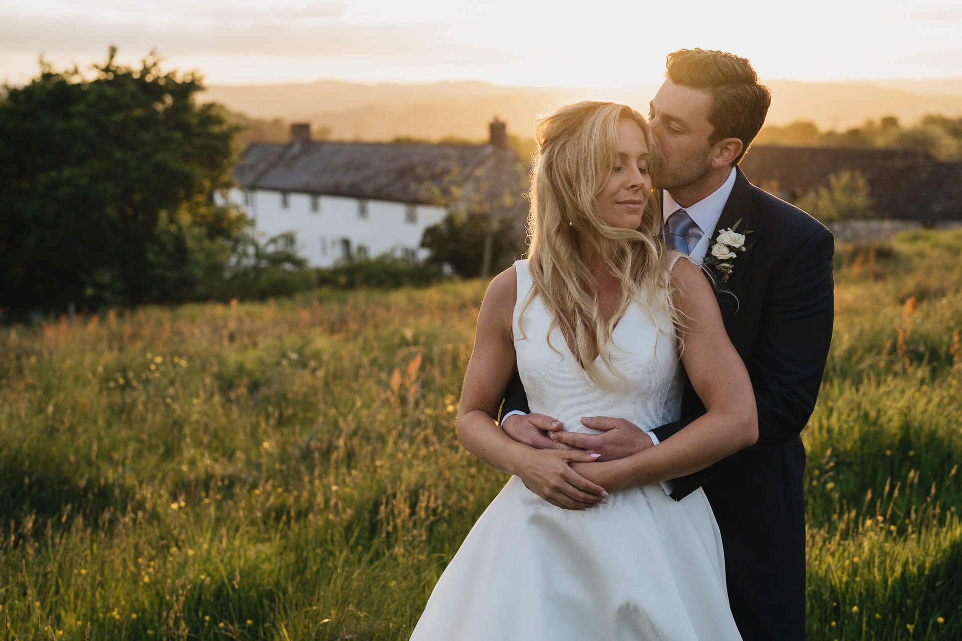 Bride and groom with River Cottage behind them and sunset over the fields