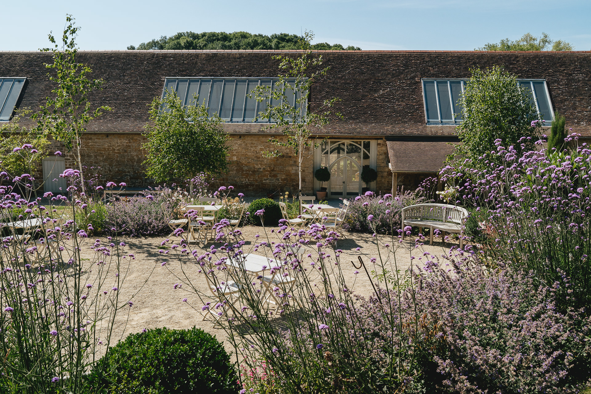 External image of the Tithe Barn, Symondsbury, ready for a wedding, with purple flowers in the foreground and blue skies above