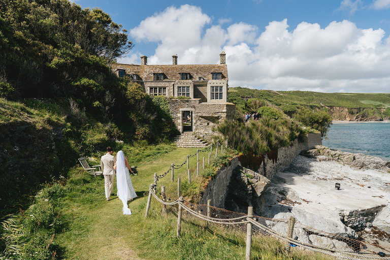 A bride and groom walking towards Porth en Alls at Prussia Cove with the sea beside them