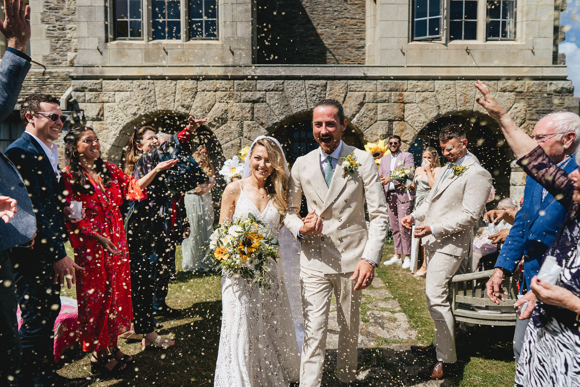 Bride and groom smiling and walking through confetti with wedding guests smiling around them