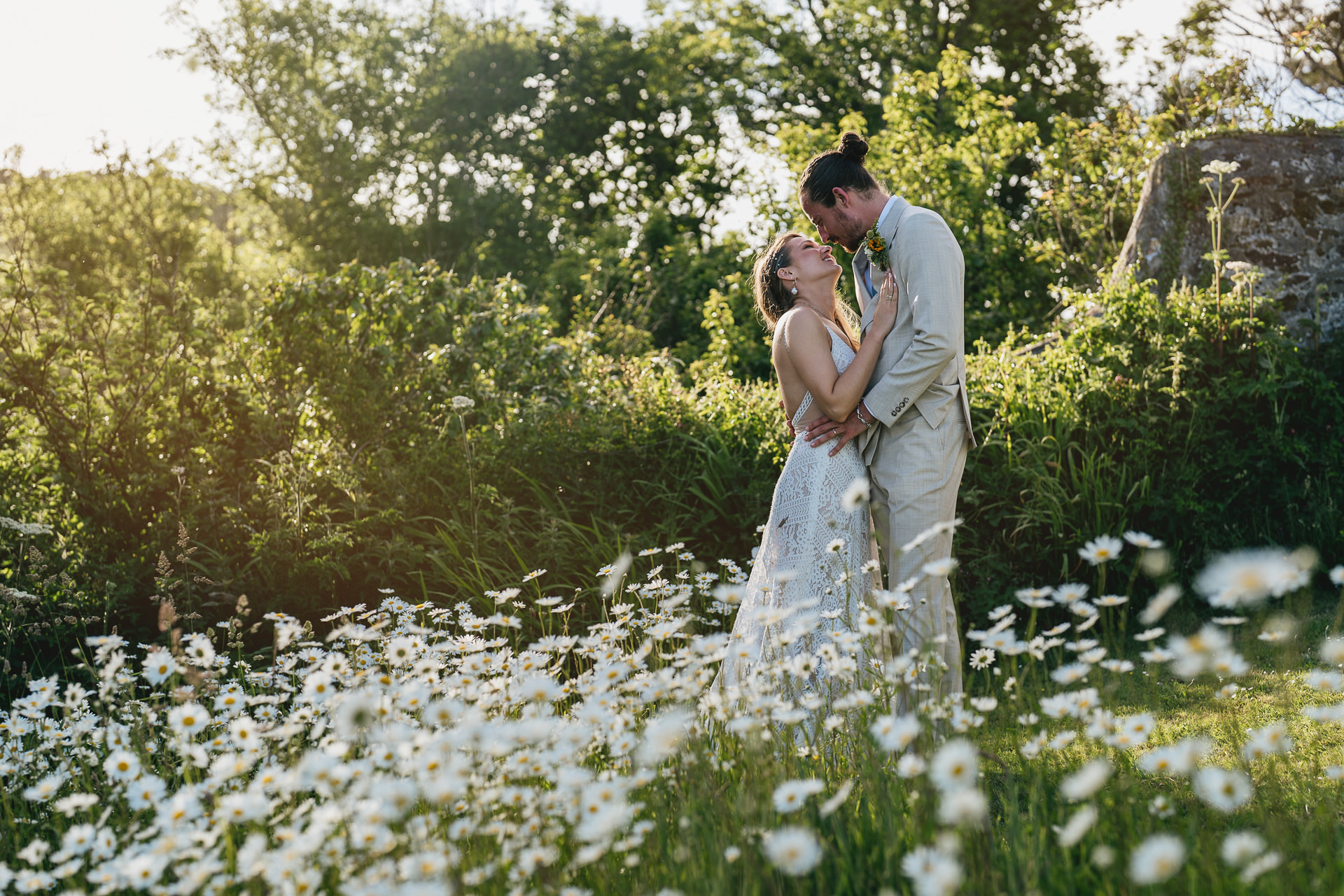 Bride and groom cuddling amongst daisies at Prussia Cove