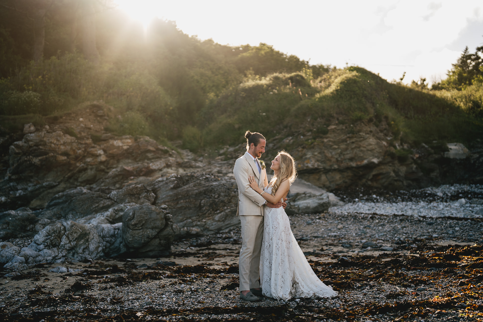 A bride and groom on the beach in Cornwall, smiling at each other