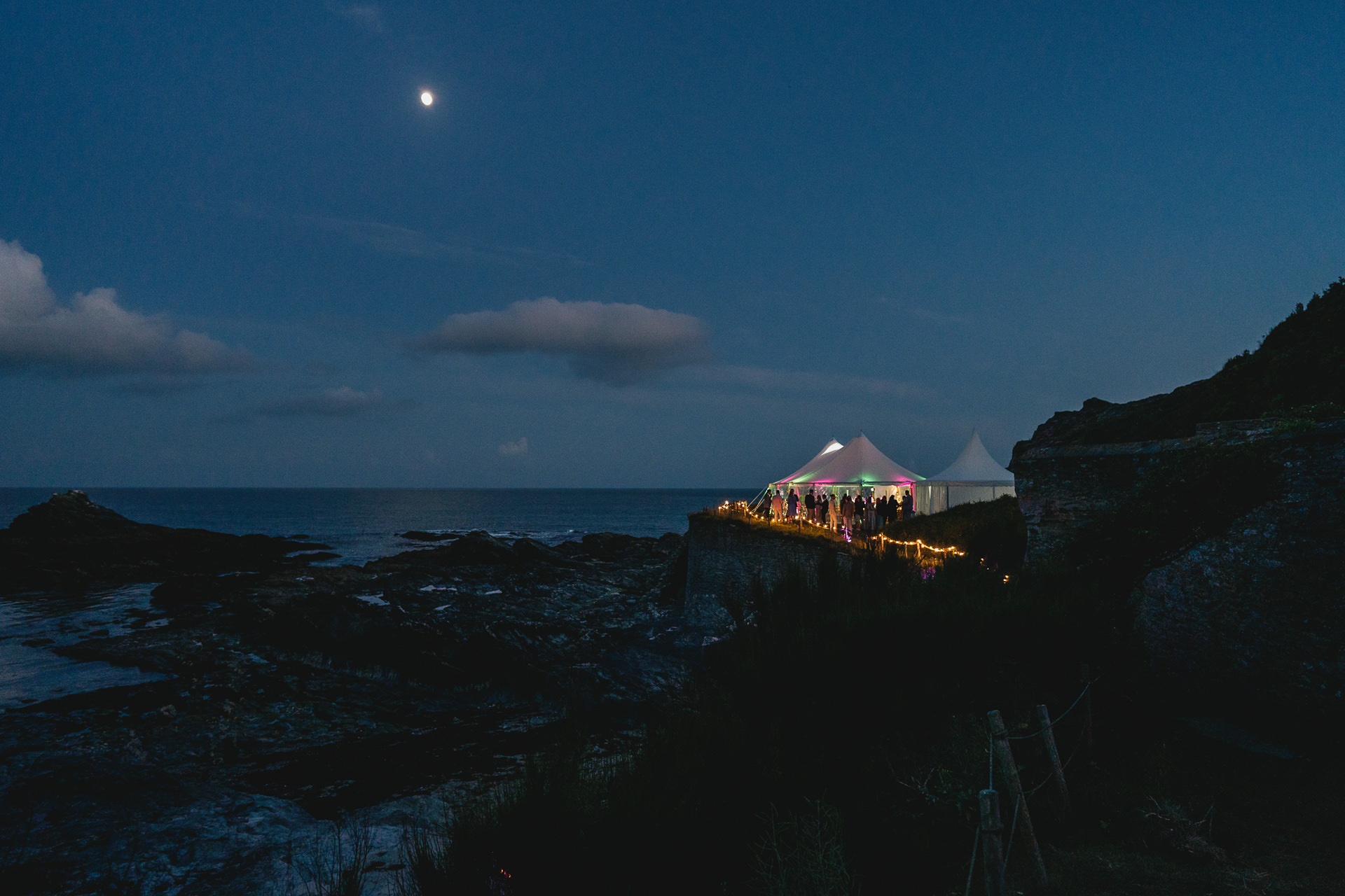 Wedding marquee at Prussia Cove in the twilight, with fairy lights leading down the pathway and the sea in the background