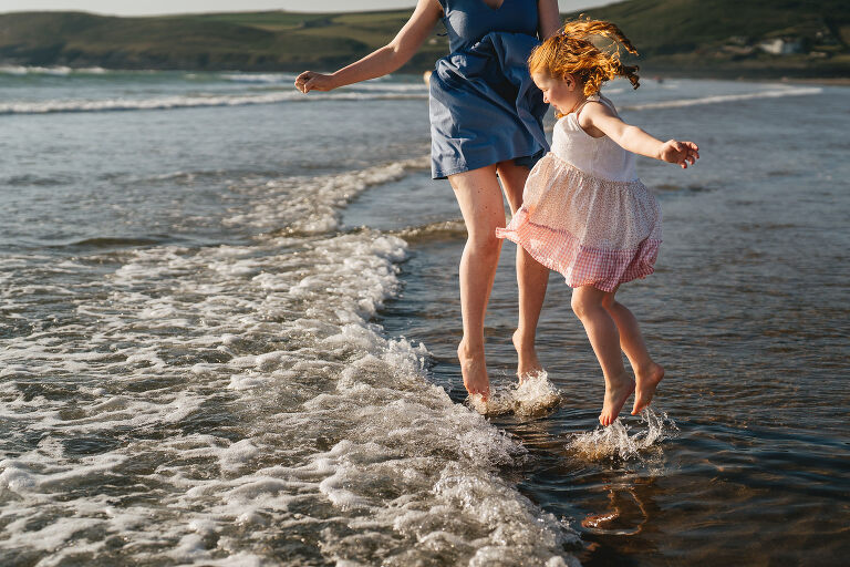 A mother and daughter jumping in the waves on the beach in North Devon