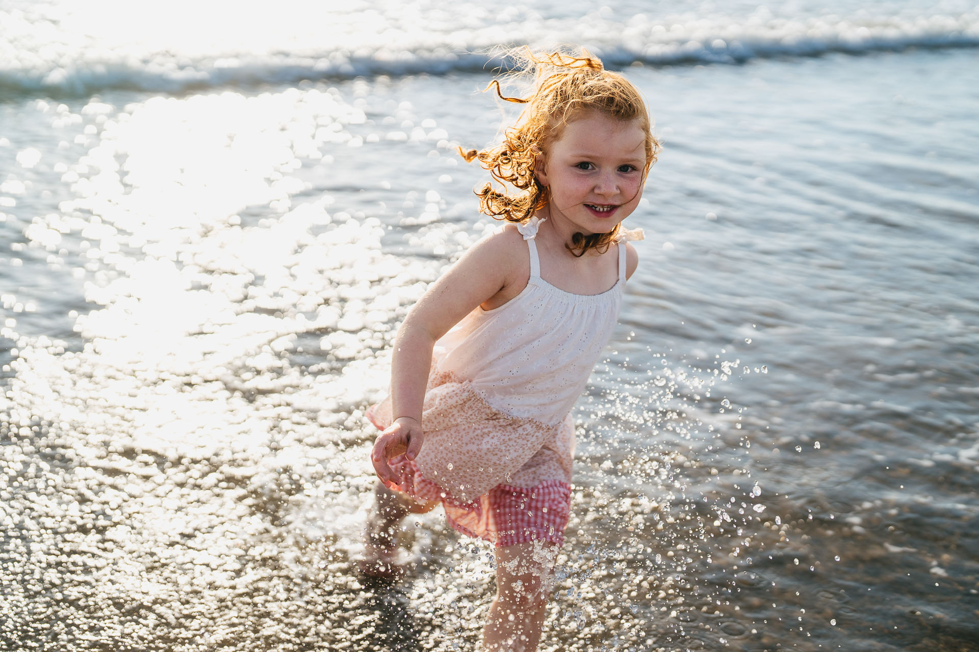 A young girl with curly hair running through the sea in North Devon