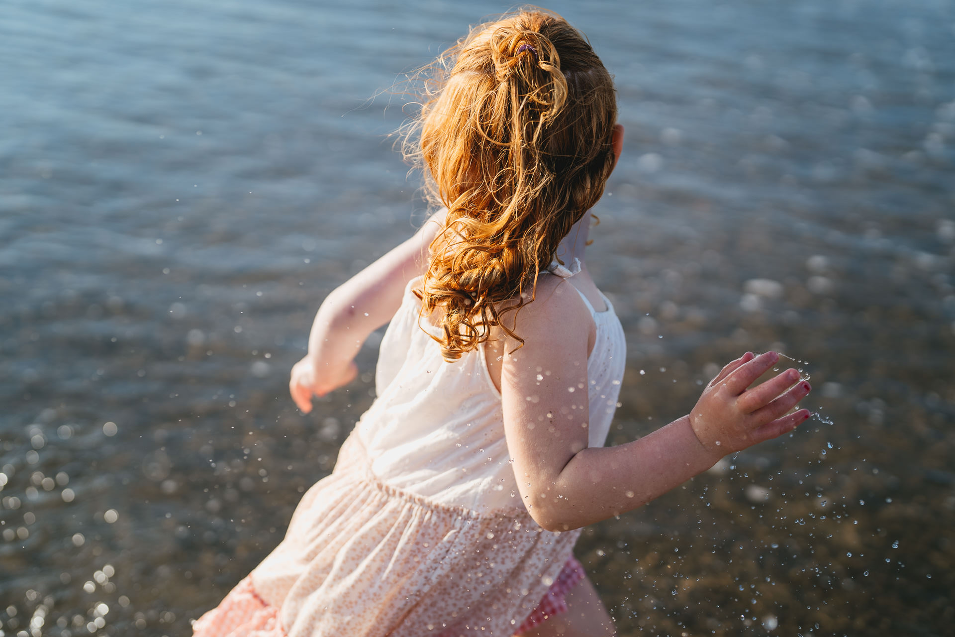 A young girl with curly hair running through the sea at Croyde beach during a family photography session