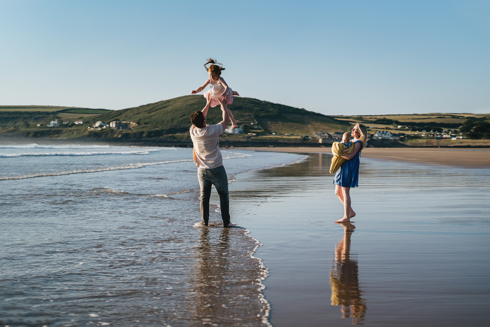 A family walking on the beach together in north Devon, with the father throwing the daughter up into the air