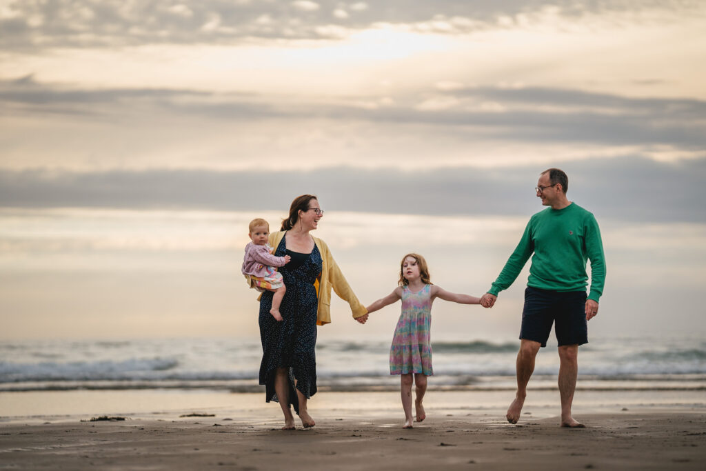 A family photo session on a beach in Devon, with four family members walking away from the sea holding hands