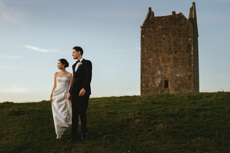 A bride and groom standing on a hill at sunset with the Bruton dovecote behind them