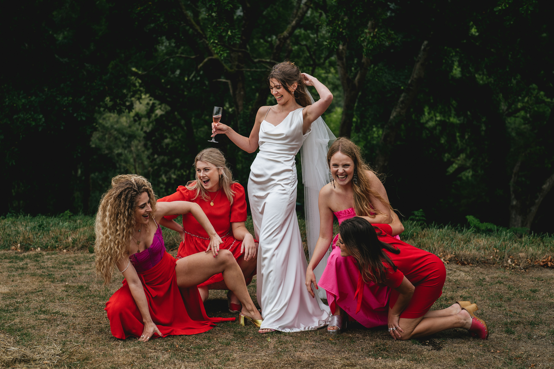 A bride in a Vivienne Westwood wedding dress surrounded by bridesmaids in stylish red and pink outfits