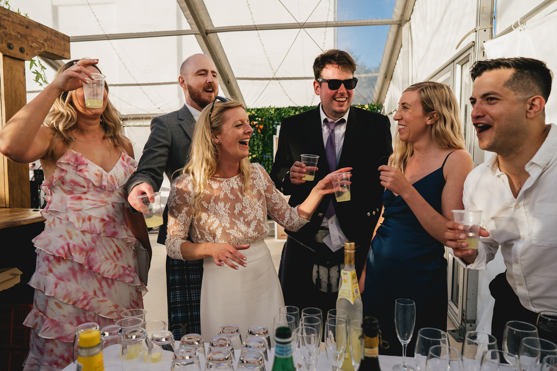 A group of wedding guests laughing together and preparing to drink shots