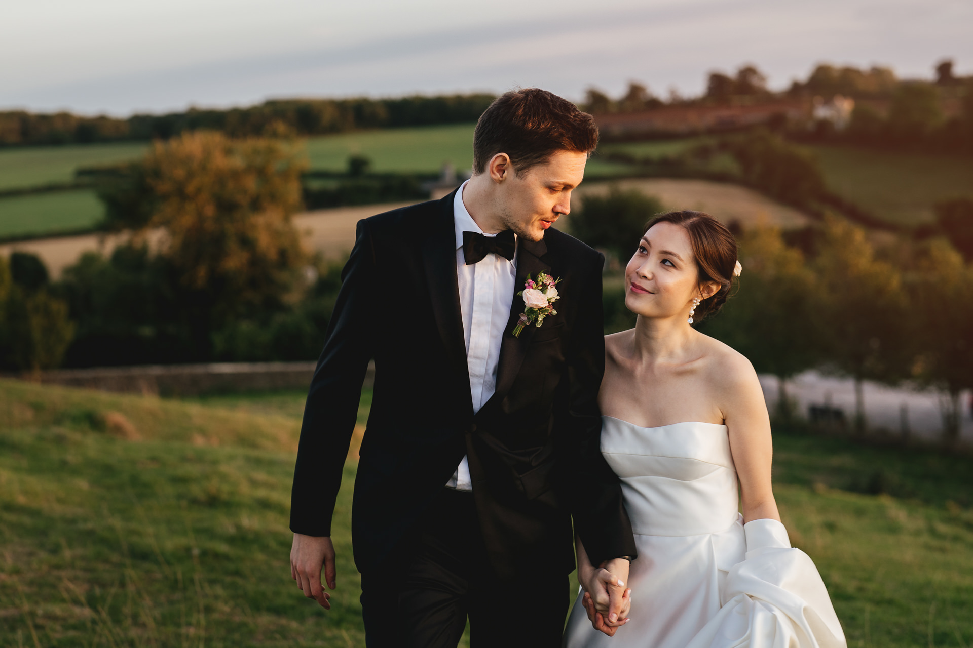 A bride and groom walking together on the hills in Somerset, hand in hand and smiling at each other