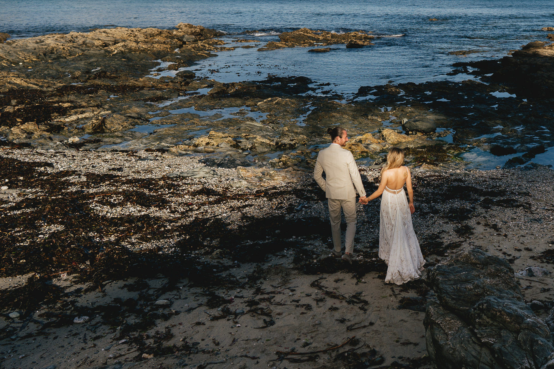 Bride and groom walking hand in hand across a rocky beach