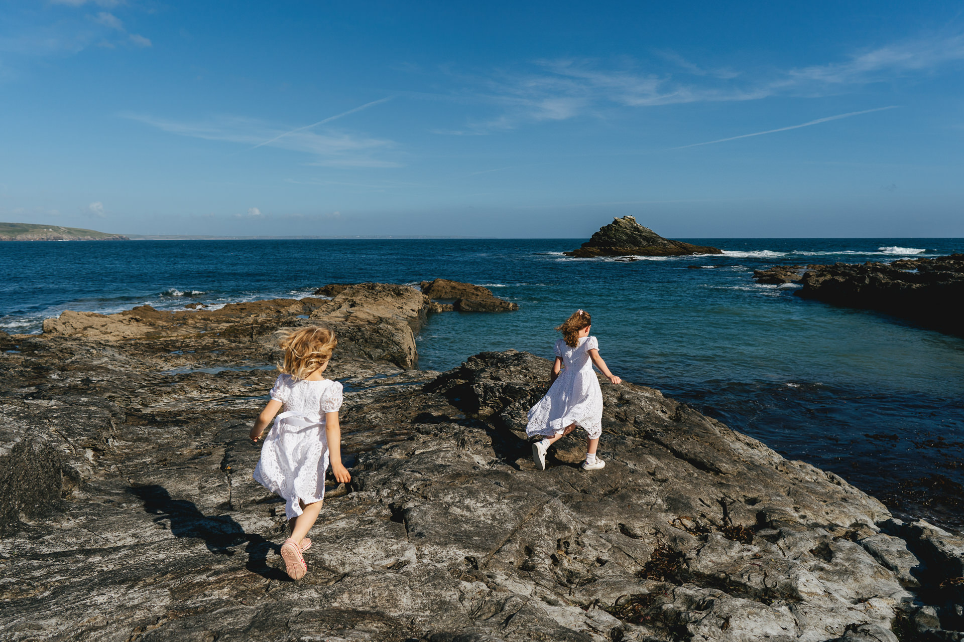 Two flower girls in white dresses playing on the rocks by the sea at Prussia Cove in Cornwall