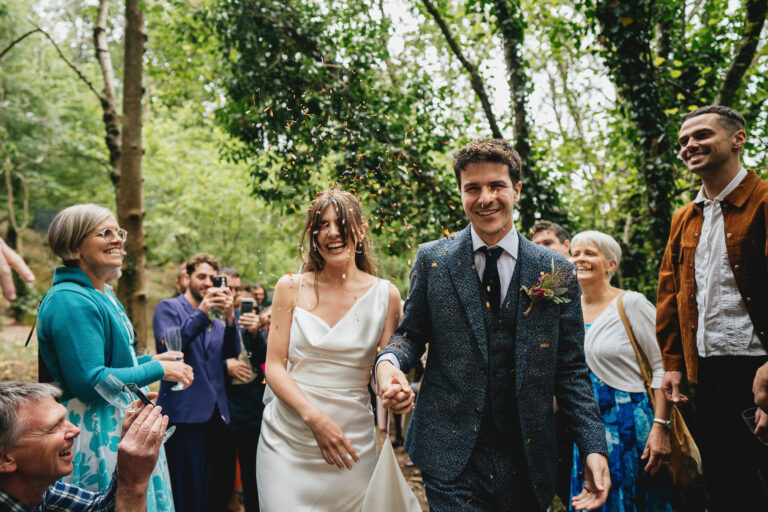 Stylish bride and groom walking through confetti during their Dartmoor woodland wedding