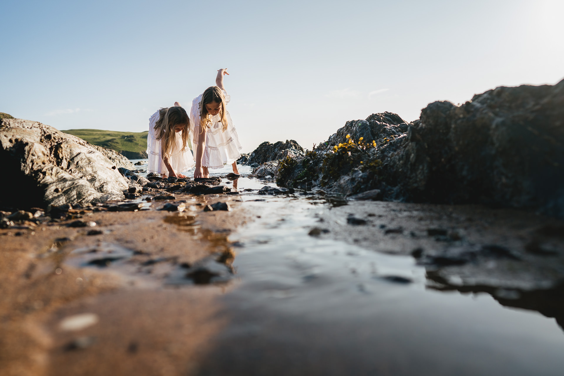 Two girls in white dresses searching for stones on the beach during an evening photography session in Devon