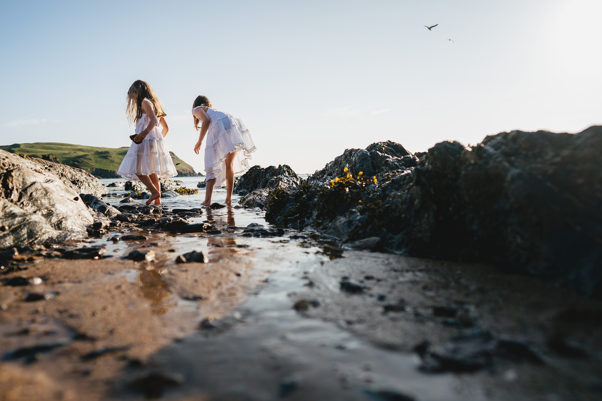 Two girls in white dresses exploring the beach in the evening