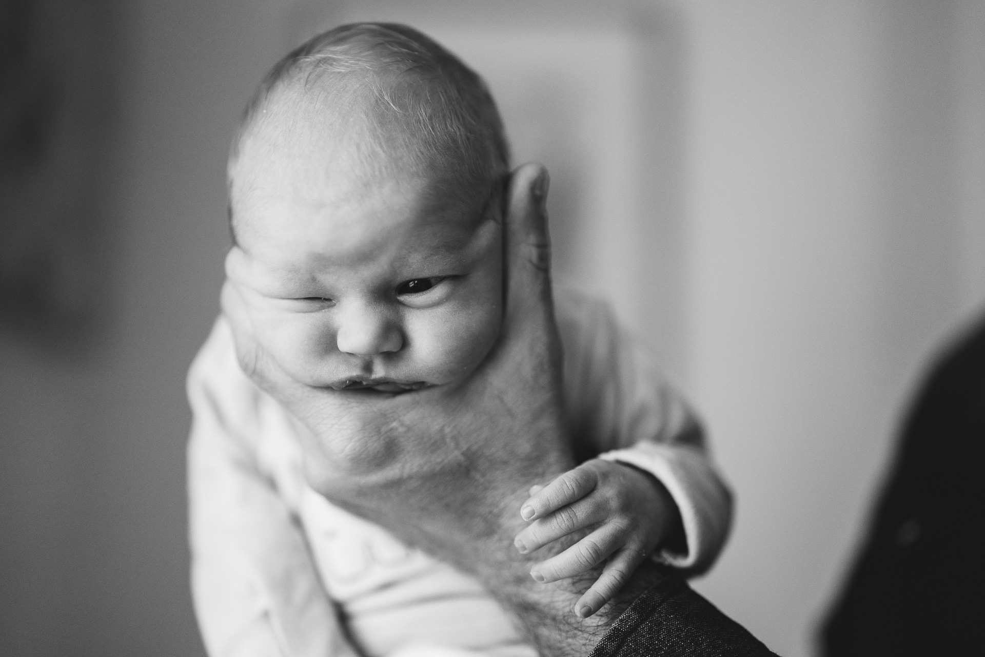 A newborn baby held in father's hands during a newborn photography session in Devon