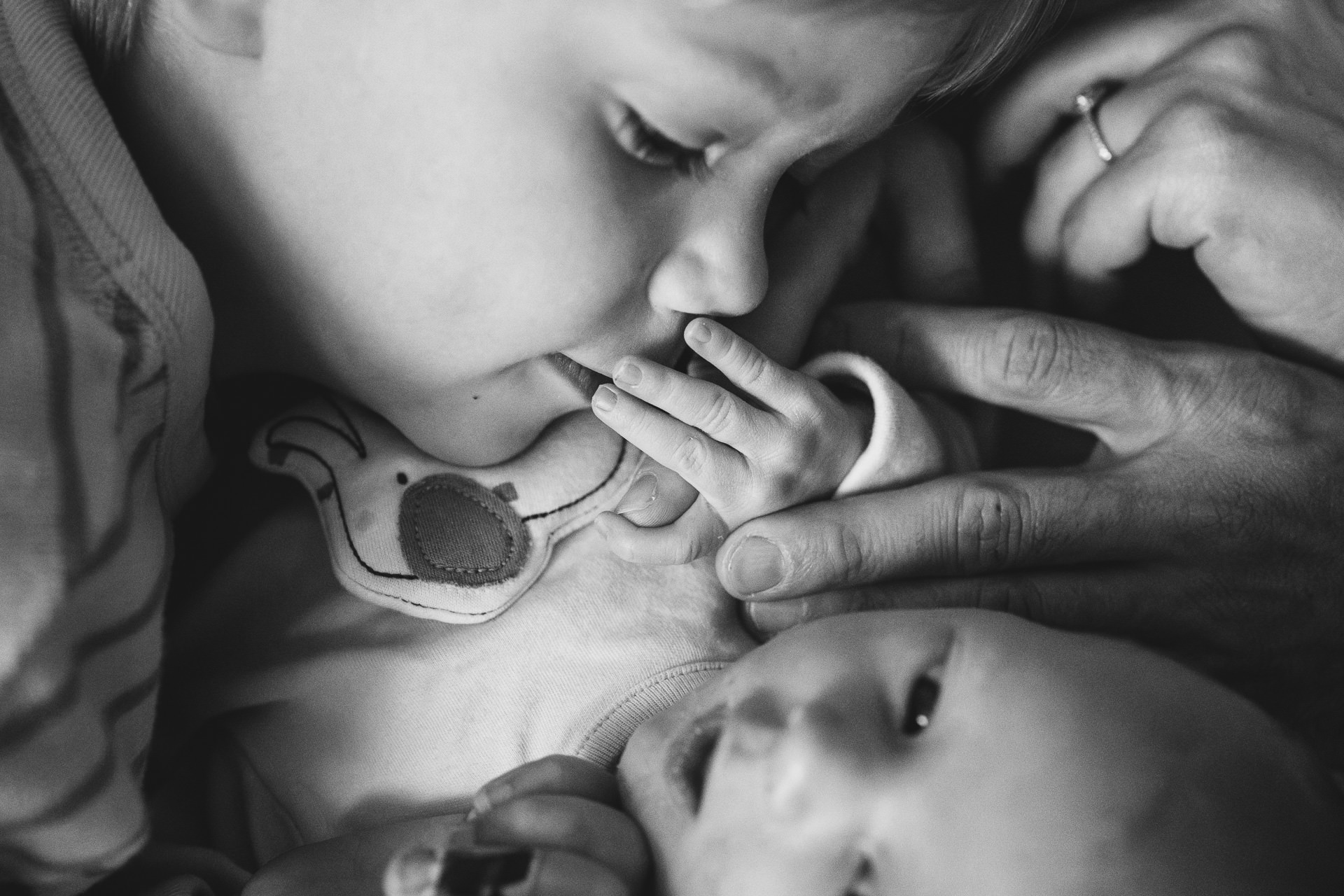 A young boy kissing a newborn baby's hand during a photo session
