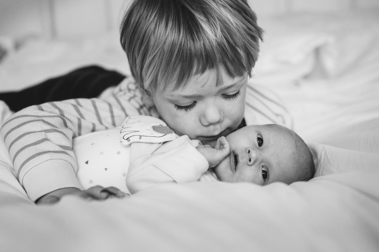 Older brother kissing a newborn baby on a bed
