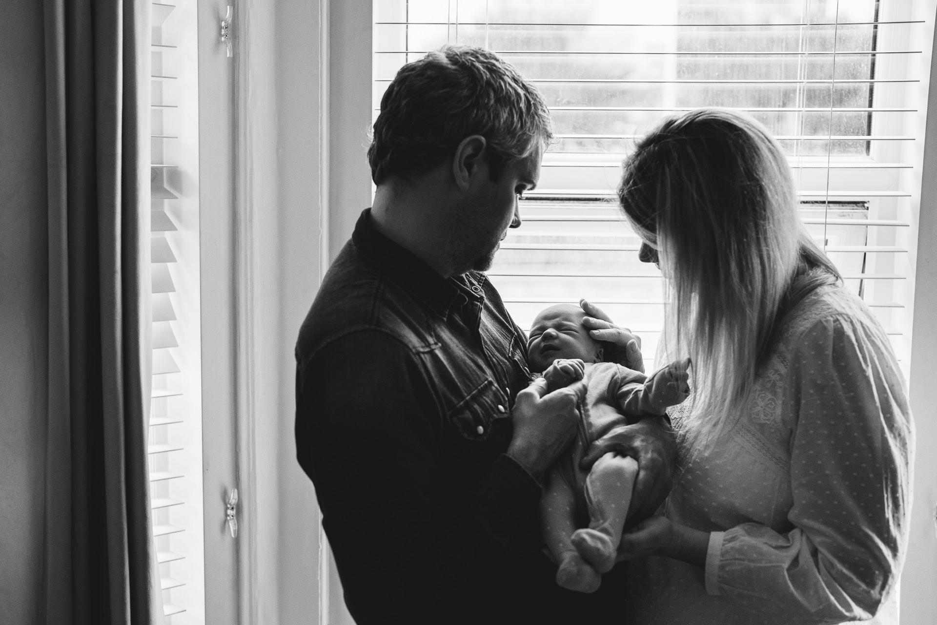 Parents standing by the window cuddling a newborn baby