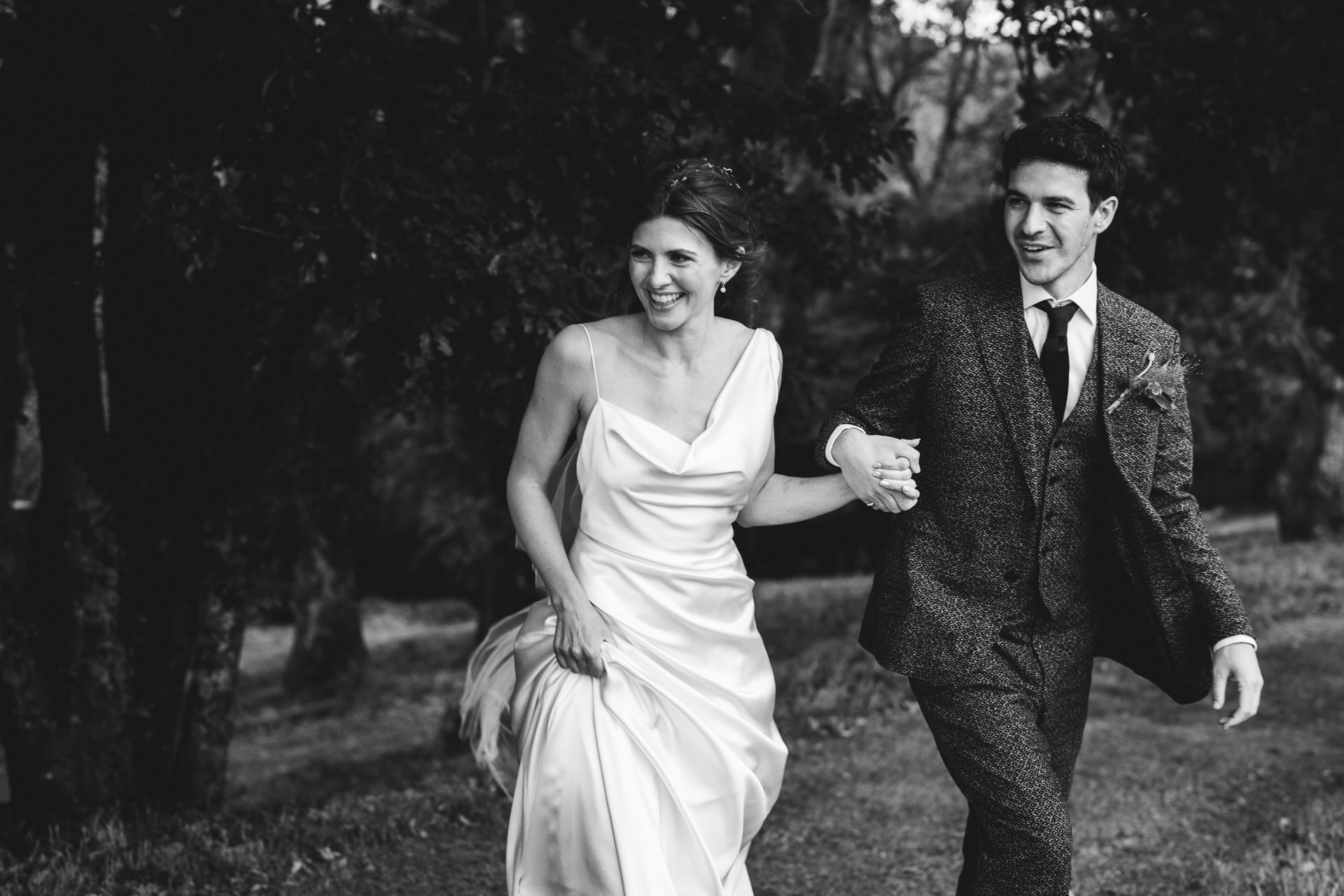 A bride in Vivienne Westwood and groom in a bespoke Casely Hayford suit walking hand in hand and smiling at a Dartmoor wedding